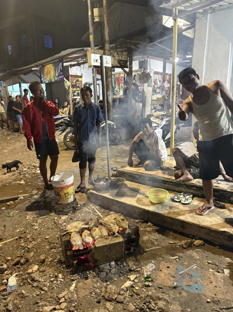 photo in North Jakarta featuring happy locals cooking fish on a homemade grill on the floor